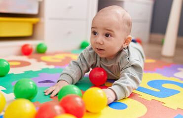 Fototapeta na wymiar Adorable caucasian baby playing with balls lying on floor at kindergarten