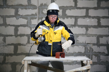 Locksmith in special clothes and goggles works in production. Worker. A man in a helmet and with a grinder in his hand. Industry. Builder. Metal processing with angle grinder
