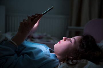 A child using smart phone lying in bed late at night, playing games, watching videos online,...