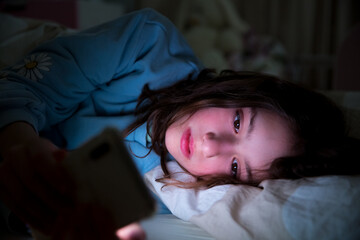 A child using smart phone lying in bed late at night, playing games, watching videos online, scrolling screen. Children's screen addiction and parent control concept. Child's room at night. 