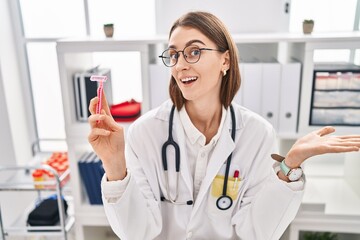 Young caucasian doctor woman holding razor celebrating achievement with happy smile and winner expression with raised hand