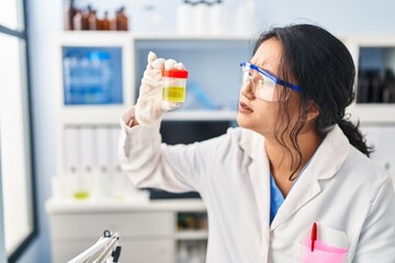 Young chinese woman wearing scientist uniform holding urine analysis test tube at laboratory