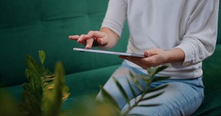 Woman touching screen of digital tablet, hands of close-up. Businesswoman sitting on couch distance works for tablet online chatting with company investors.