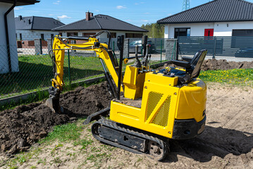 Mini digger digging a hole in the garden along the fence to the drainage pipes.