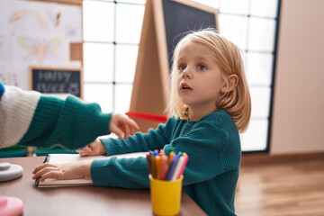 Adorable caucasian boy sitting on table with relaxed expression at kindergarten