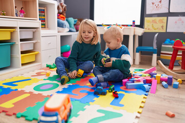 Adorable boy and girl playing with cars toy sitting on floor at kindergarten