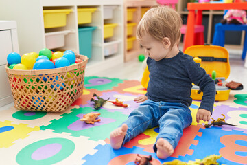Fototapeta na wymiar Adorable blond toddler playing with dino toys sitting on floor at kindergarten