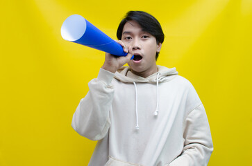 Shocked and surprised asian man shouting through paper megaphone giving an announcement.
