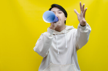 Shocked and surprised asian man shouting through paper megaphone giving an announcement.