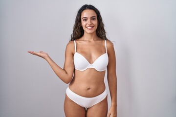Fototapeta premium Young hispanic woman wearing white lingerie smiling cheerful presenting and pointing with palm of hand looking at the camera.