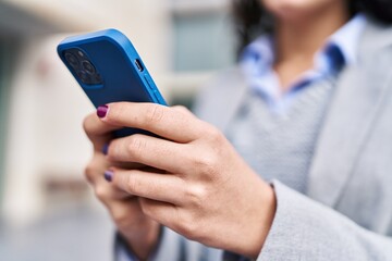 Young hispanic woman executive using smartphone at street