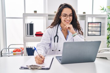 Young hispanic woman wearing doctor uniform using laptop working at clinic