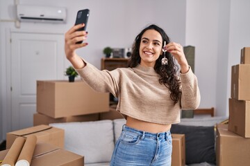 Young hispanic woman make selfie by the smartphone holding key at new home