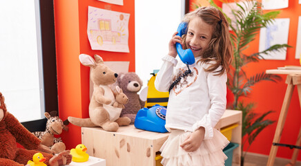 Adorable hispanic girl playing telephone toy standing at kindergarten