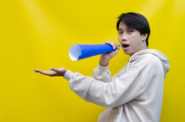 Asian man pointing finger and promoting something while shouting to paper megaphone. best for sale, discount, and promotion content
