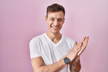 Caucasian man standing over pink background clapping and applauding happy and joyful, smiling proud...