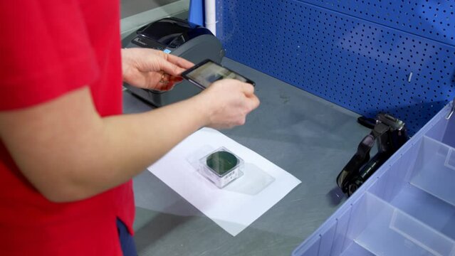 Young woman takes photos of product for fixation and archivation put on white piece of paper near label printer. Registration of goods