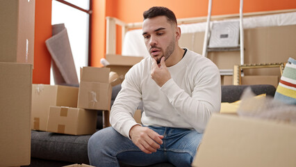 Young hispanic man sitting on sofa with serious expression at new home