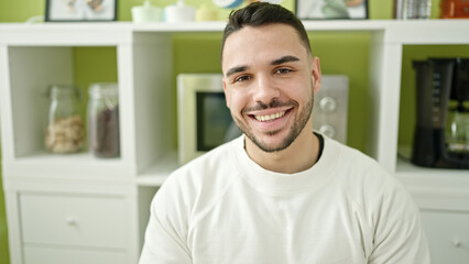 Young hispanic man smiling confident sitting on table at dinning room