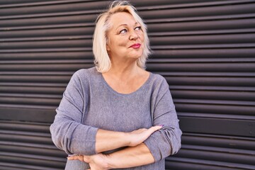 Middle age blonde woman smiling confident standing with arms crossed gesture at street