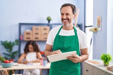 Middle age hispanic man painting on art notebook with pencils winking looking at the camera with...