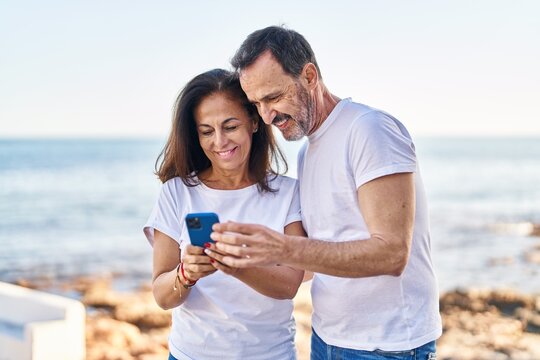 Middle age man and woman couple using smartphone standing together at seaside - Powered by Adobe