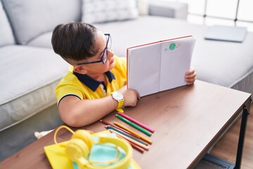 Adorable hispanic boy showing notebook with draw sitting on floor at home