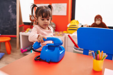 Adorable hispanic girl playing telephone toy sitting on table at kindergarten