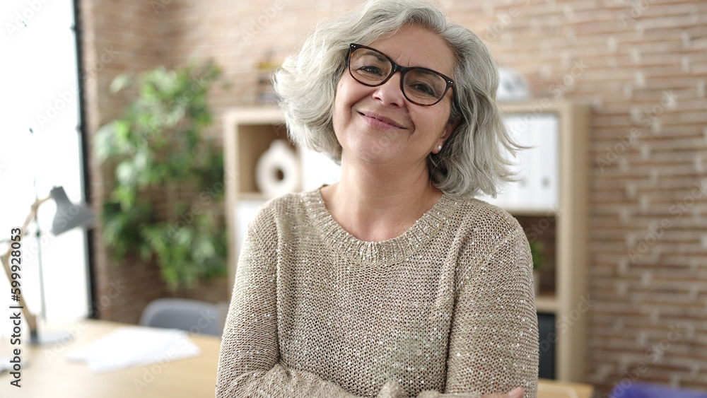 Sticker Middle age woman with grey hair business worker smiling confident standing with arms crossed gesture at office