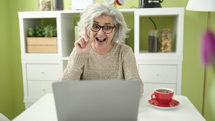 Middle age woman with grey hair having video call sitting on table at home