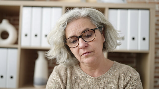 Middle age woman with grey hair business worker sitting with relaxed expression at office