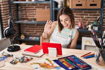 Fototapeta premium Young beautiful hispanic woman artist having video call sitting on table at art studio