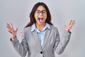 Hispanic young business woman wearing glasses celebrating mad and crazy for success with arms...