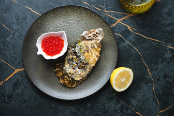 Olive plate with fresh unopened oyster and red caviar, flat lay on a dark-olive marble background, horizontal shot
