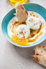 Turquoise bowl with turkish cilbir and flatbread on a light-beige stone background, middle close-up, vertical shot, selective focus