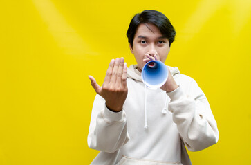 Shocked and surprised asian man shouting through paper megaphone giving an announcement.