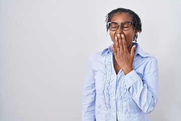 African woman with dreadlocks standing over white background wearing glasses bored yawning tired covering mouth with hand. restless and sleepiness.