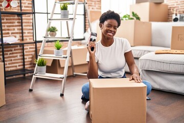 African american woman packing cardboard box sitting on floor at new home