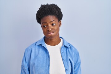 African american woman standing over blue background puffing cheeks with funny face. mouth inflated with air, crazy expression.