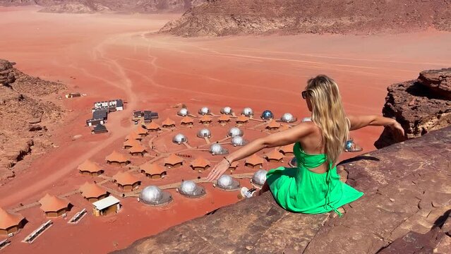 a girl sits on the edge of a desert cliff in front of a bubble hotel in wadi rum desert - 14 jun 2022