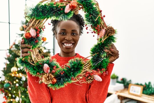 African american woman smiling confident holding christmas wreaths decor at home