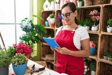 Young beautiful hispanic woman florist smiling confident using touchpad at flower shop