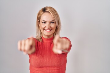 Blonde woman standing over isolated background pointing to you and the camera with fingers, smiling positive and cheerful