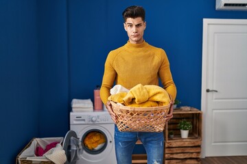 Young hispanic man holding laundry basket skeptic and nervous, frowning upset because of problem....