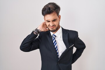 Young hispanic man with tattoos wearing business suit and tie suffering of neck ache injury, touching neck with hand, muscular pain