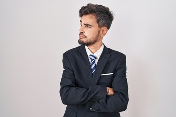 Young hispanic man with tattoos wearing business suit and tie looking to the side with arms crossed convinced and confident