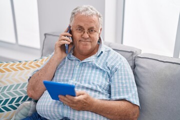 Middle age grey-haired man talking on smartphone using touchpad at home