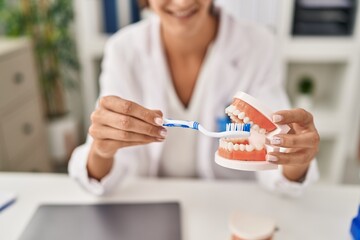 Young beautiful hispanic woman dentist teaching to clean tooth at clinic