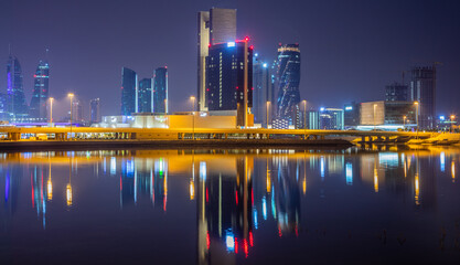 Manama illuminated downtown reflected in the water on the shore of Persian gulf, Manama, Bahrain