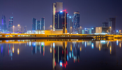 Obraz premium Manama illuminated downtown reflected in the water on the shore of Persian gulf, Manama, Bahrain